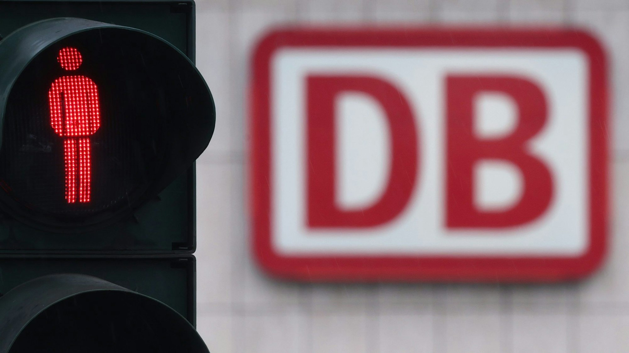 Das Logo der Deutschen Bahn am Gebäude des Hauptbahnhofs ist hinter einer auf Rot stehenden Fußgängerampel zu sehen.