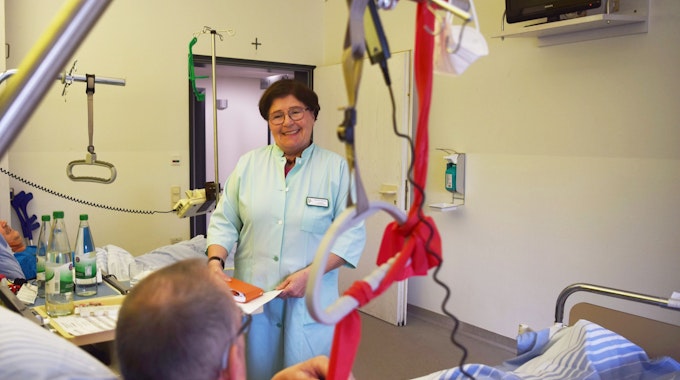 Marianne Kesseler steht in einem grünen Kittel am Bett eines Patienten in einem Zwei-Bett-Zimmer der Unfallstation im Kreiskrankenhaus Mechernich.