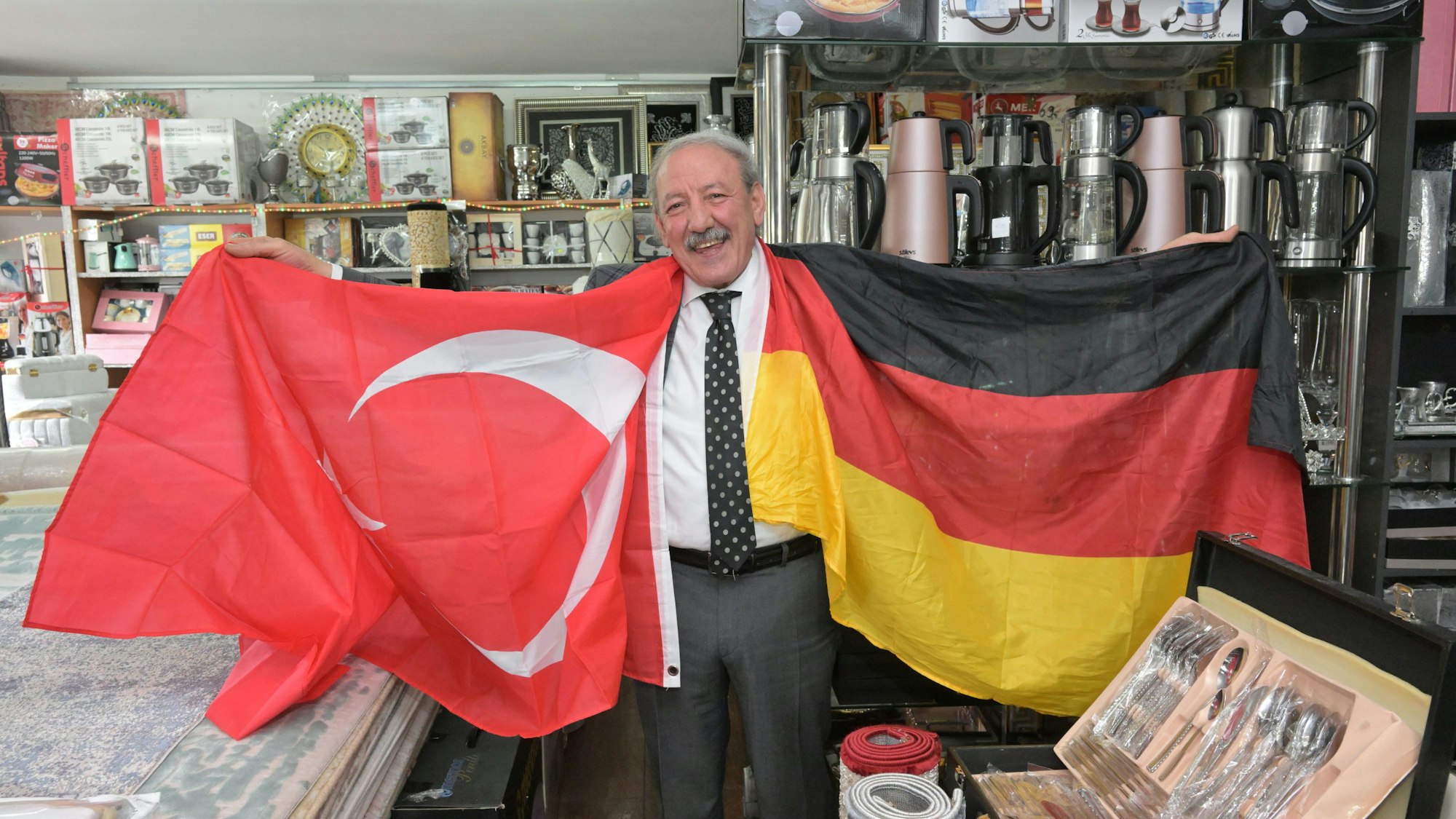 Hasan Ata, Inhaber des  Teppichgeschäfts Gonau. Er hält zwei Fahnen in den Händen, eine türkische und eine deutsche.