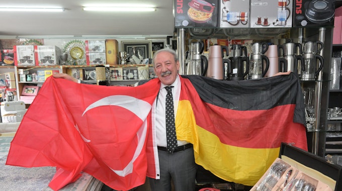 Hasan Ata, Inhaber des  Teppichgeschäfts Gonau. Er hält zwei Fahnen in den Händen, eine türkische und eine deutsche.