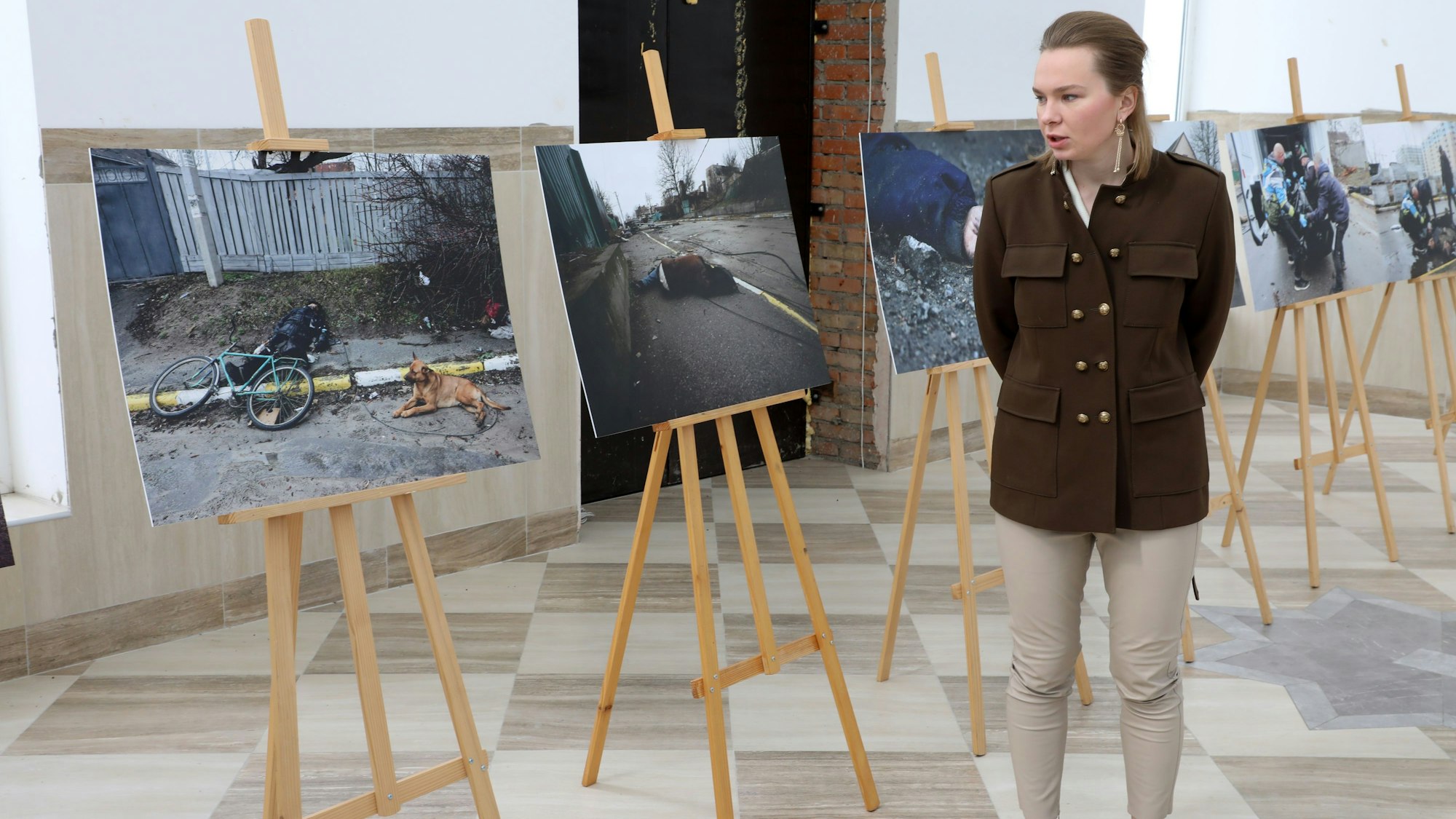 Eine Frau erklärt Bilder, auf denen auf offener Straße erschossene Zivilisten in Butscha zu sehen sind.