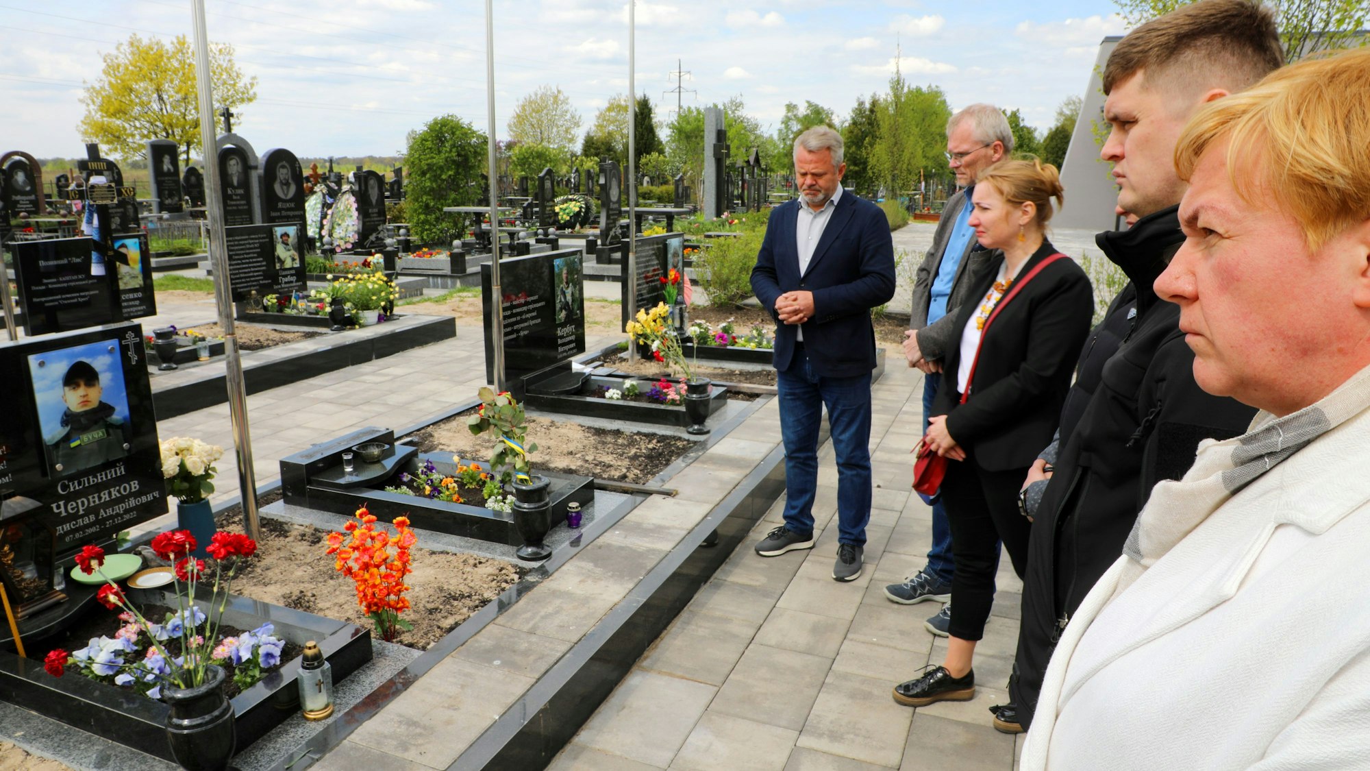 Menschen stehen an Gräbern, auf deren Grabsteine Bilder ukrainischer Soldaten zu sehen sind.