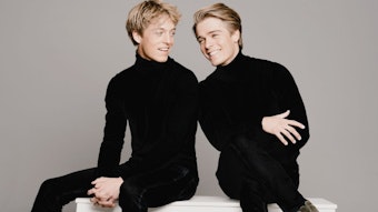 Lucas und Arthus Jussen sitzen beide ganz in schwarz gekleidet auf einer weißen Bank.