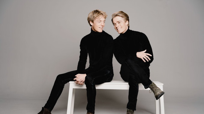 Lucas und Arthus Jussen sitzen beide ganz in schwarz gekleidet auf einer weißen Bank.