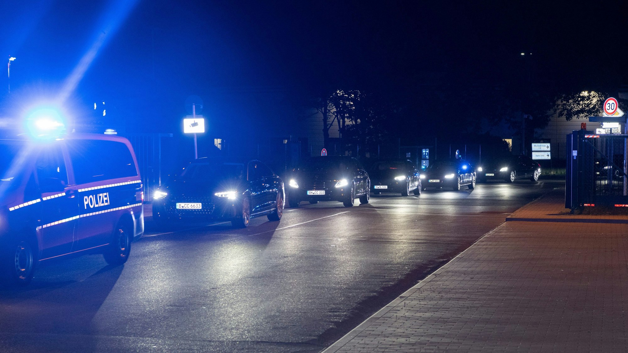 Ein Konvoi mit Einsatzfahrzeugen der Polizei, Limousinen und gepanzerten Fahrzeugen fährt auf einer Straße.