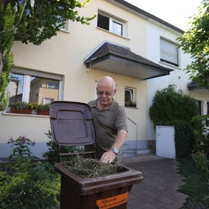 Ein Mann greift vor einem Haus in eine Mülltonne.