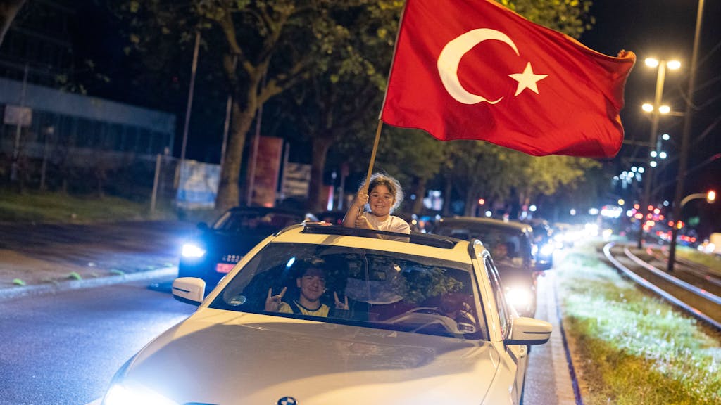 Ein Mädchen hält aus einem fahrenden Auto eine Türkei-Flagge und freut sich