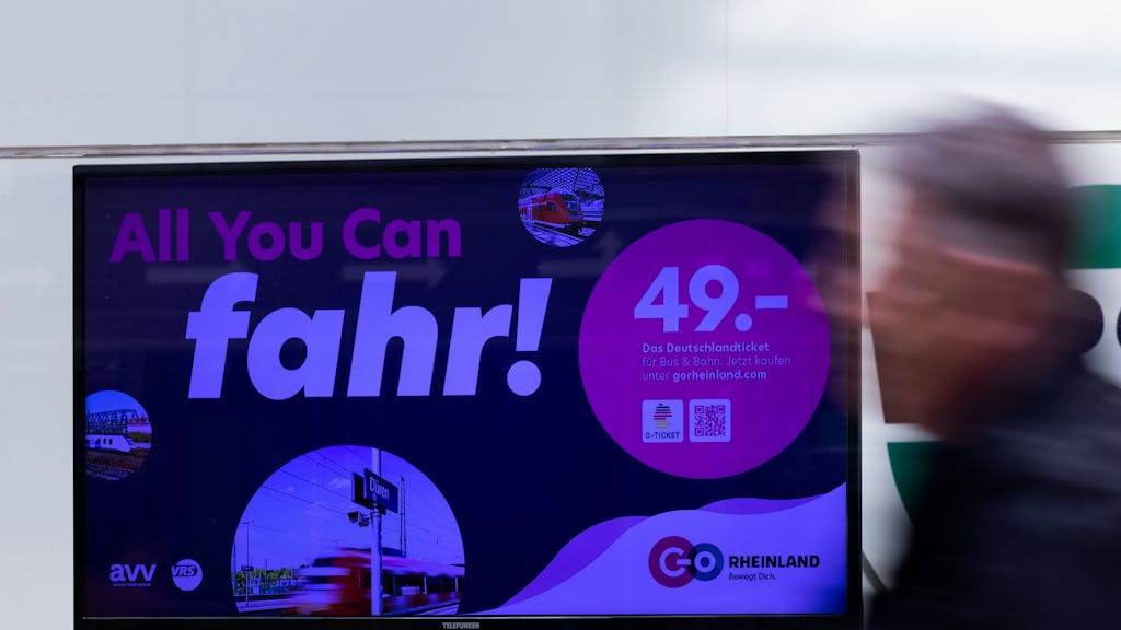 „All you can fahr“ steht auf einem Monitor als Werbung für das Deutschlandticket.