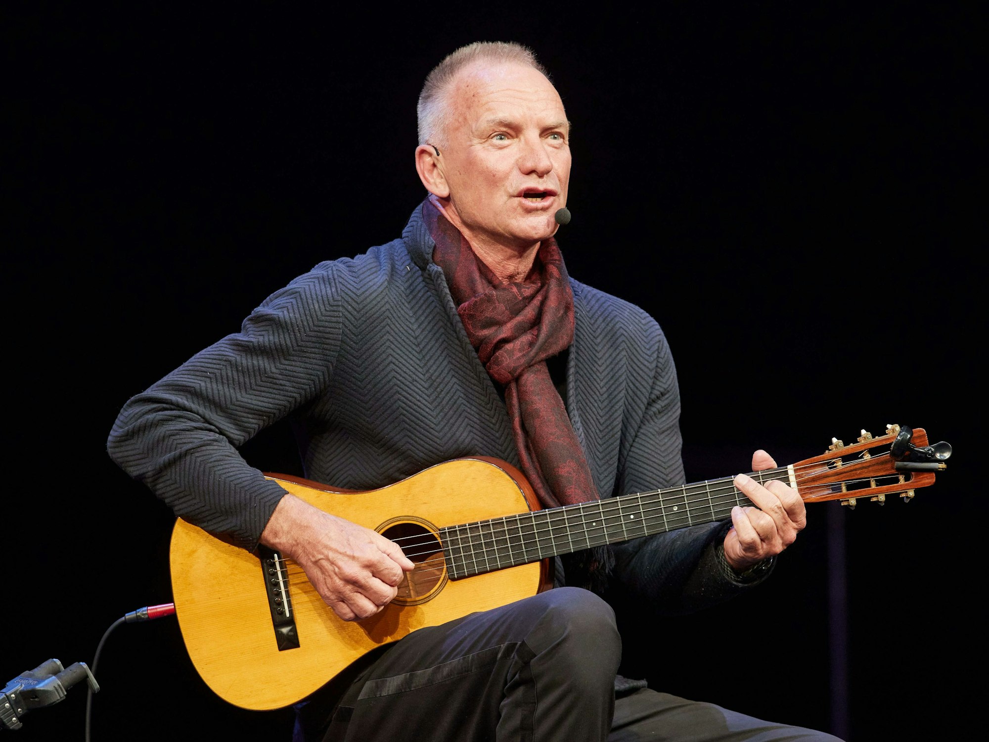 Sting sitzt und spielt Gitarre.