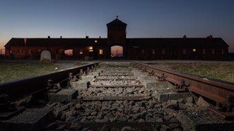 Blick von Eisenbahnschienen auf das Eingangsportal des ehemaligen Konzentrationslagers Auschwitz-Birkenau.