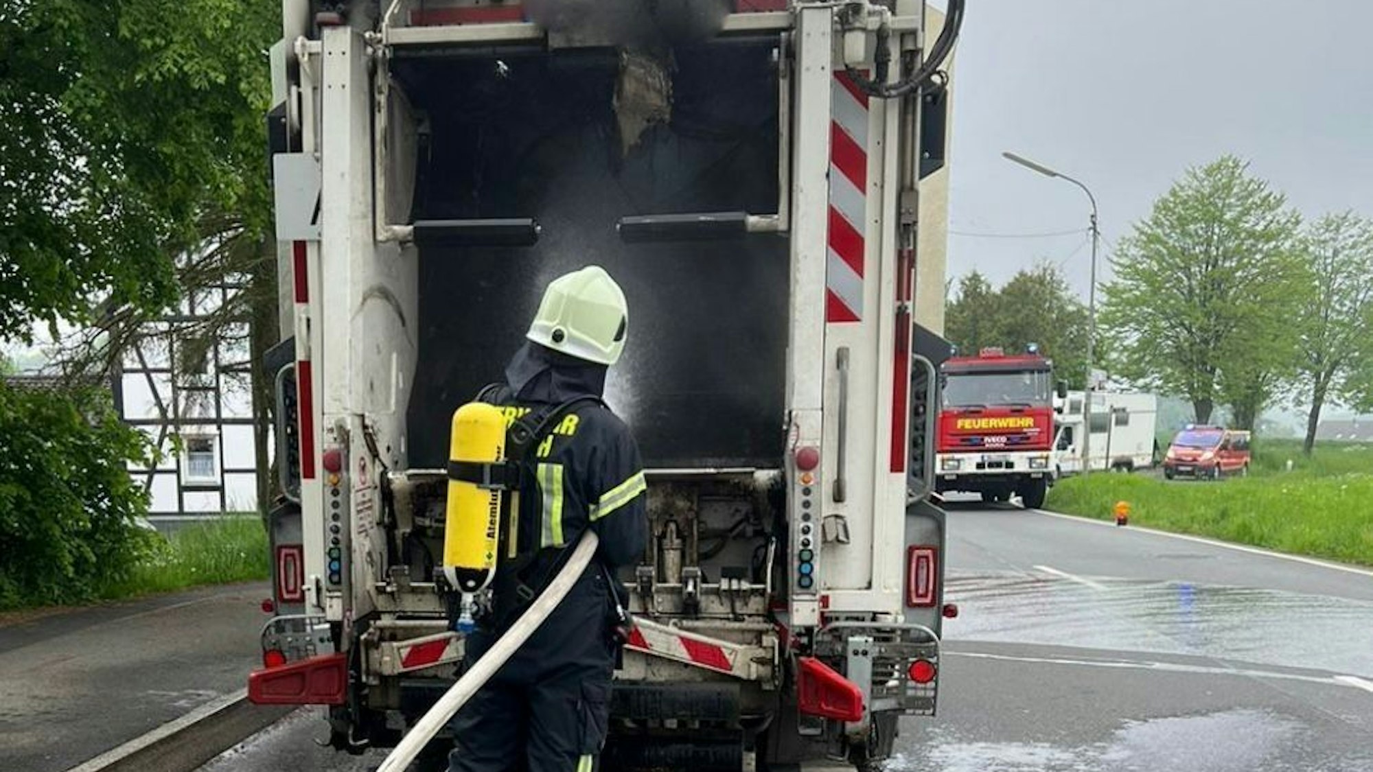 Ein Feuerwehrmann mit Atemschutzausrüstung löscht ein brennendes Müllfahrzeug.