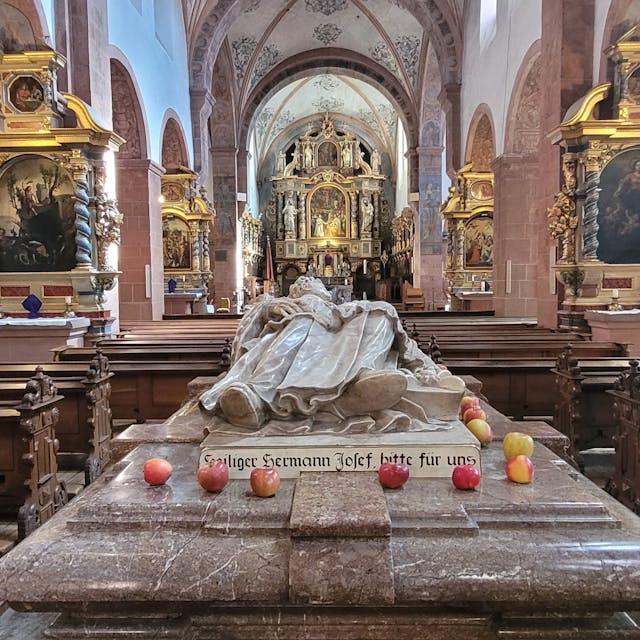 Blick auf den Marmorsarkophag der heiligen Hermann Josef, auf dem einige Äpfel liegen.