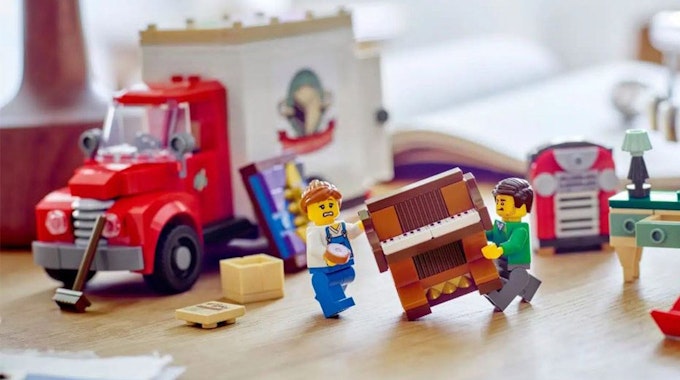 Das Set Lego Umzugswagen (40586) mit zwei Lego Minifiguren, die ein Klavier transportieren.