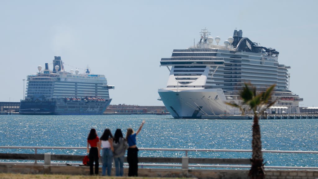 Menschen spazieren an der Meerespromenade in der Nähe eines Schiffs der Flotte „Mein Schiff“ und des Kreuzfahrtschiffes „MSC Seaview“.