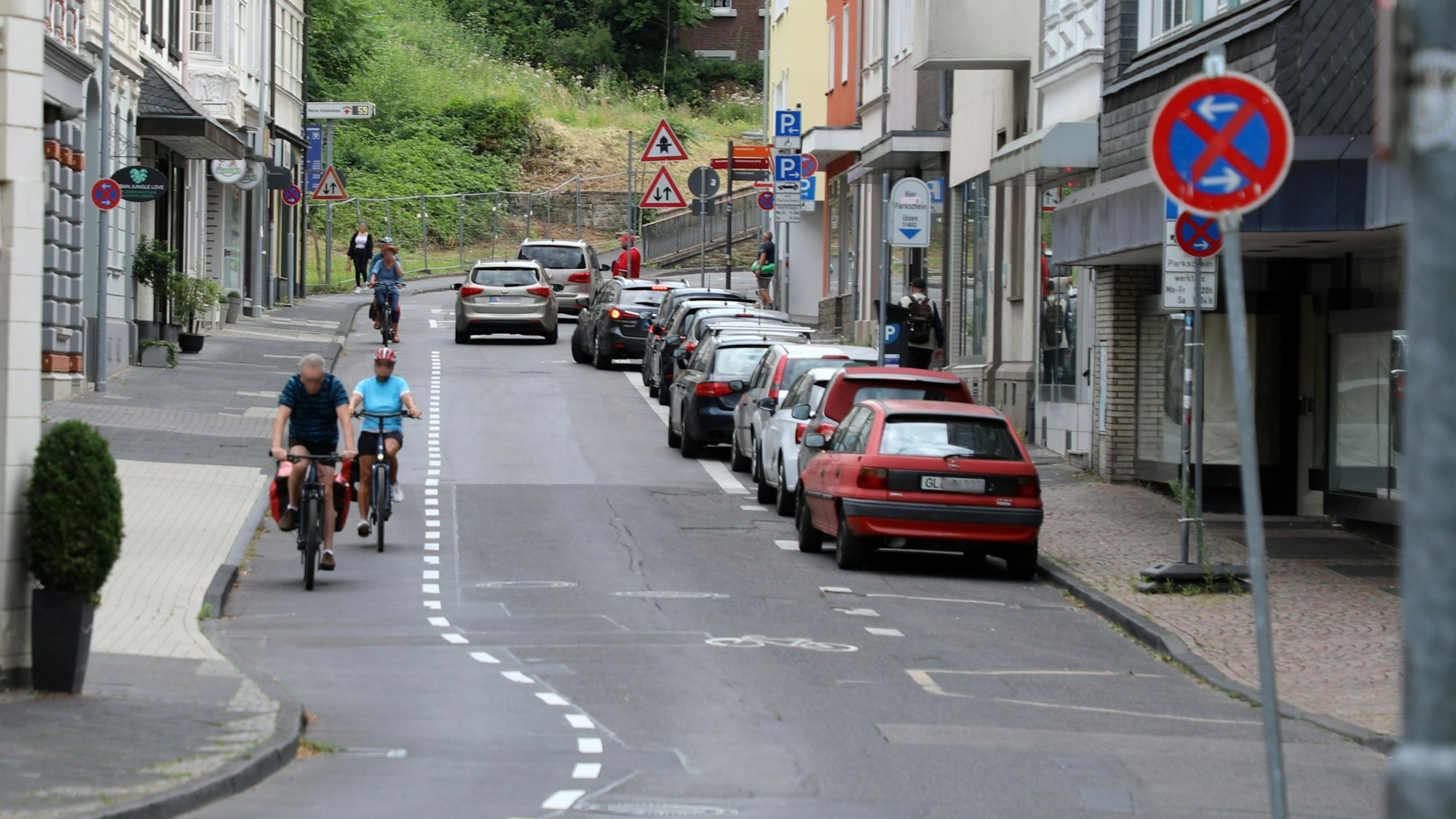 Links auf dem Foto sind Radfahrer auf dem Radstreifen unterwegs. Auf dem Parkstreifen rechts im Bild parken Autos. Auf der Fahrbahn in der Mitte fahren Autos. 