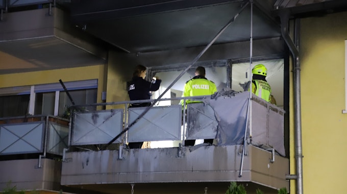 Einsatzkräfte der Polizei stehen auf dem Balkon und untersuchen den Brandherd.