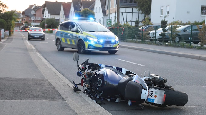 Ein Motorrad liegt auf einer Straße. Im Hintergrund steht ein Polizeiauto.
