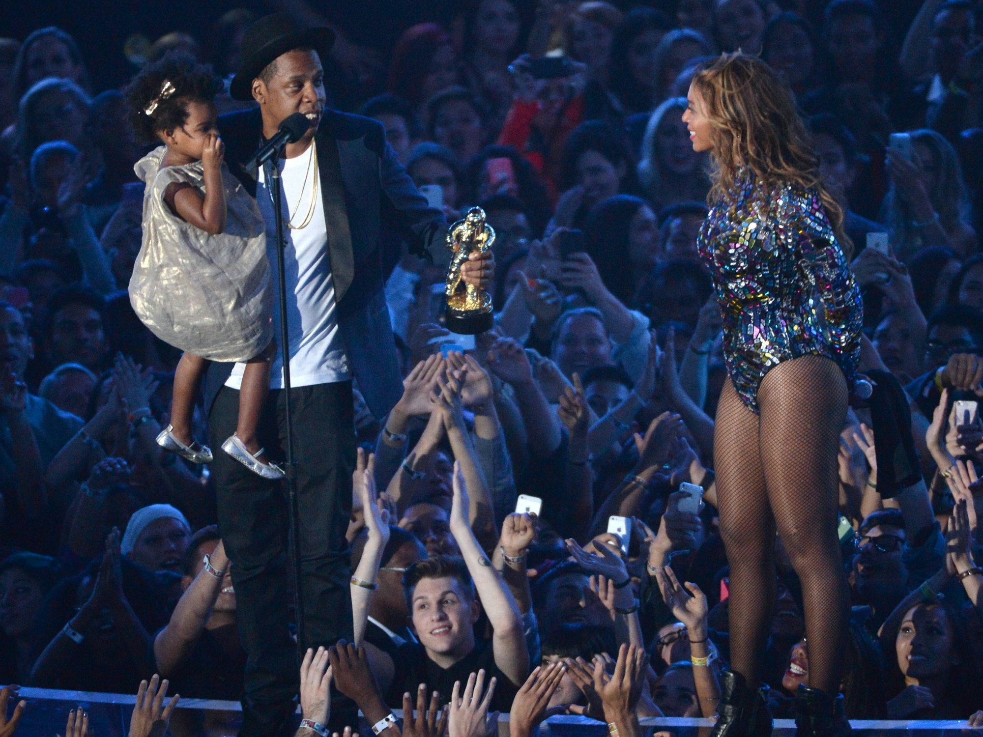 Jay-Z hat Tocter Blue Ivy auf dem Arm, Beyoncé steht daneben und lacht die beiden an.