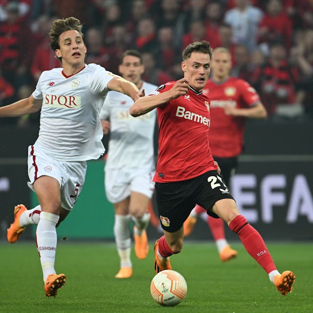 Roms Edoardo Bove in einem weißen Trikot (l) und Leverkusens Florian Wirtz in rot kämpfen um den Ball.