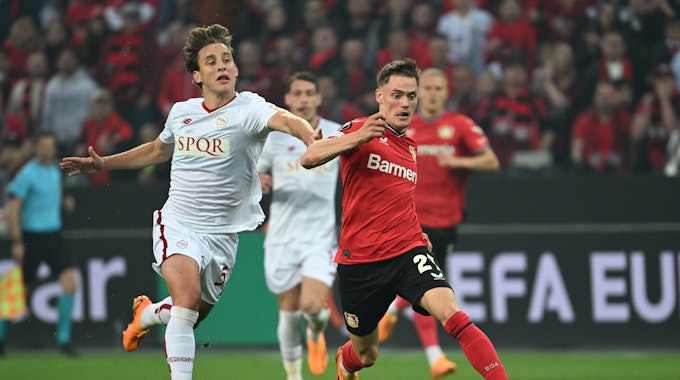 Roms Edoardo Bove in einem weißen Trikot (l) und Leverkusens Florian Wirtz in rot kämpfen um den Ball.