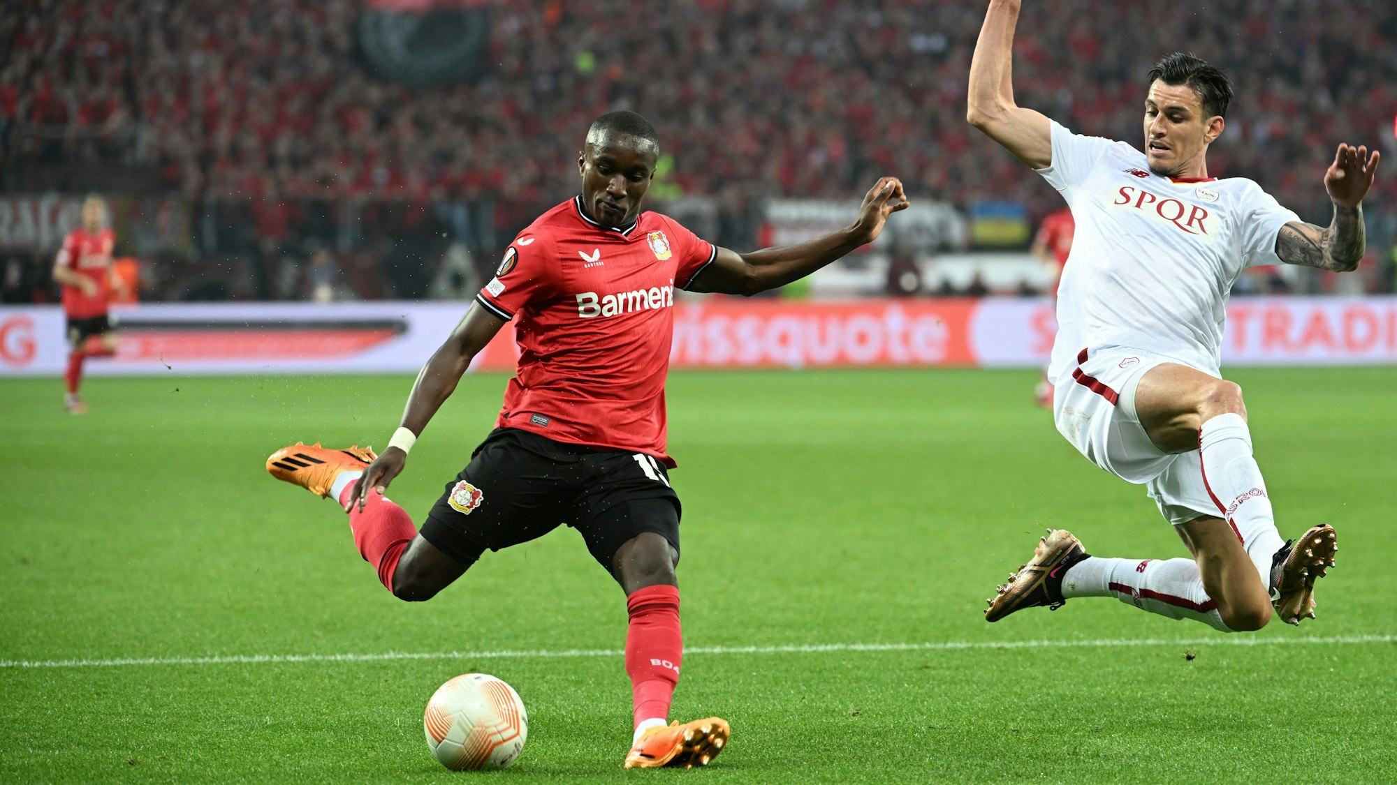 Ein Spieler von AS Rom wirft sich in einen Schuss von Leverkusens Moussa Diaby, der ein rotes Trikot trägt.