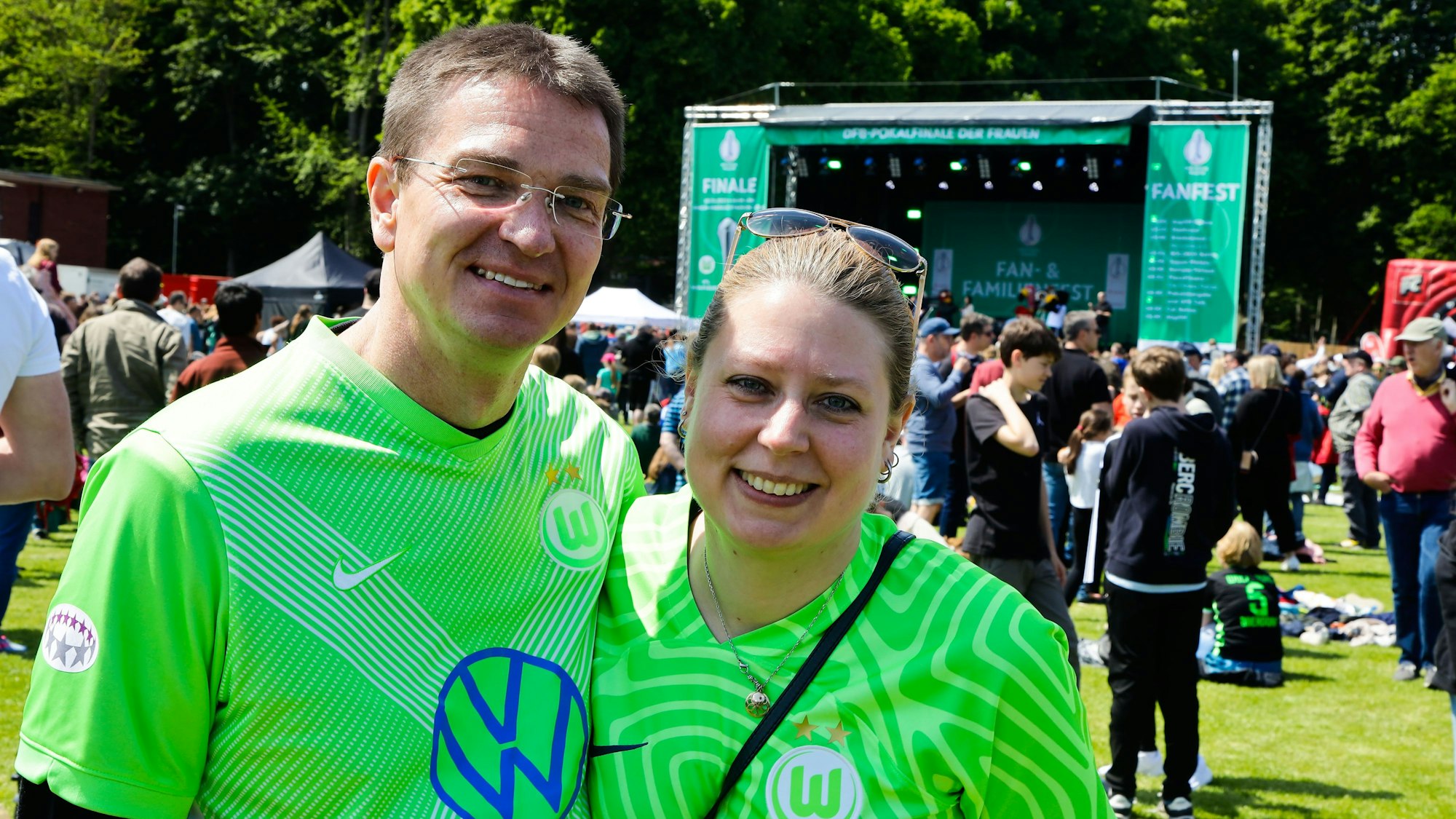 Zwei Fans des VfL Wolfsburg stehen vor einer Bühne.