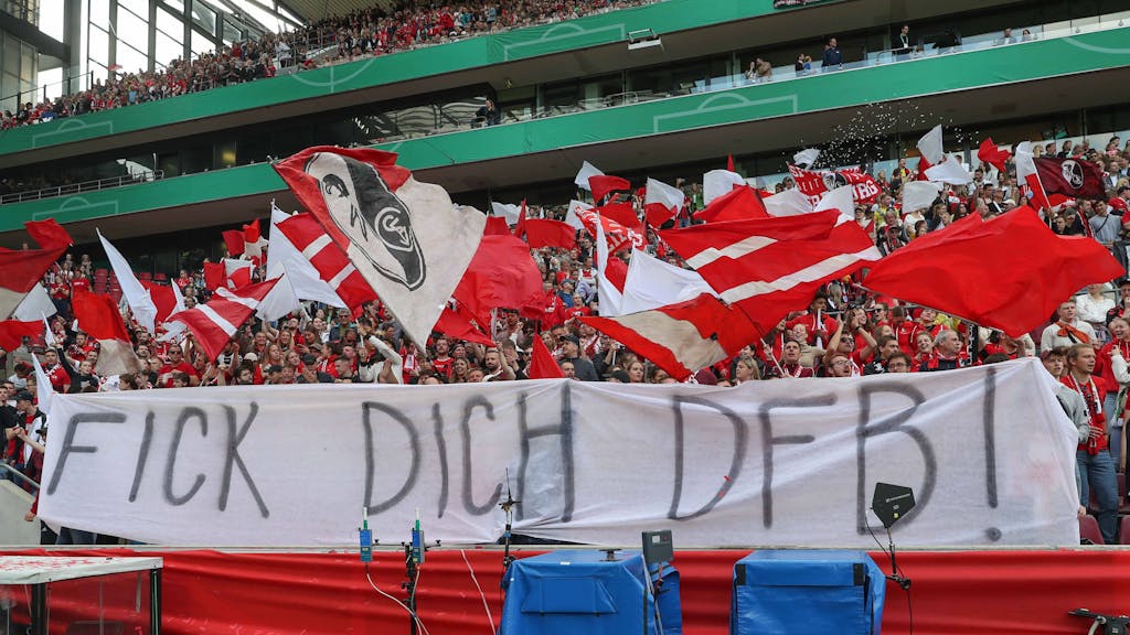 Die Fans des SC Freiburg schwenken Fahnen und präsentieren ein kritisches DFB-Banner.