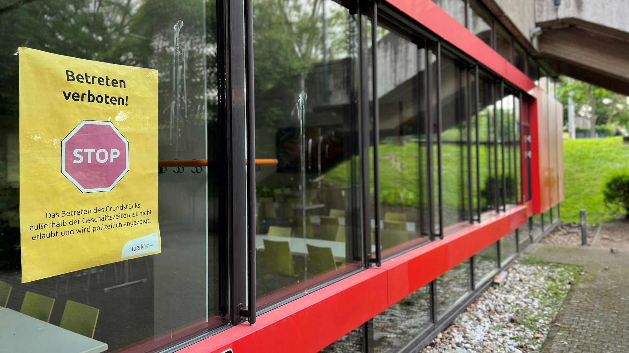 An einer Glasscheibe der Mensa hängt ein Plakat, auf dem darüber informiert wird, dass das Gelände nach Betriebsschluss nicht mehr betreten werden darf.