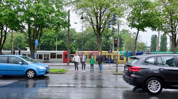 Vier Personen stehen an einer Kreuzung, auf der Straße fahren Autos.