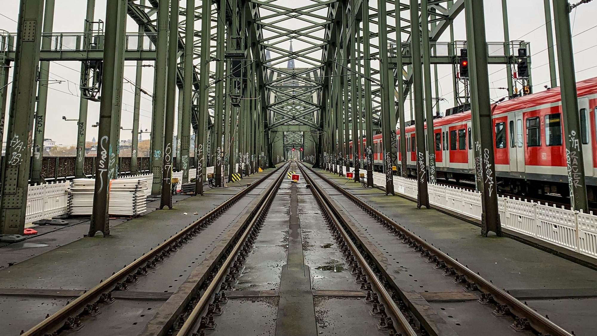 Die Gleise der Kölner Hohenzollernbrücke. Im Hintergrund ist der Kölner Dom zu sehen, rechts fährt eine S-Bahn vorbei. (Symbolbild)