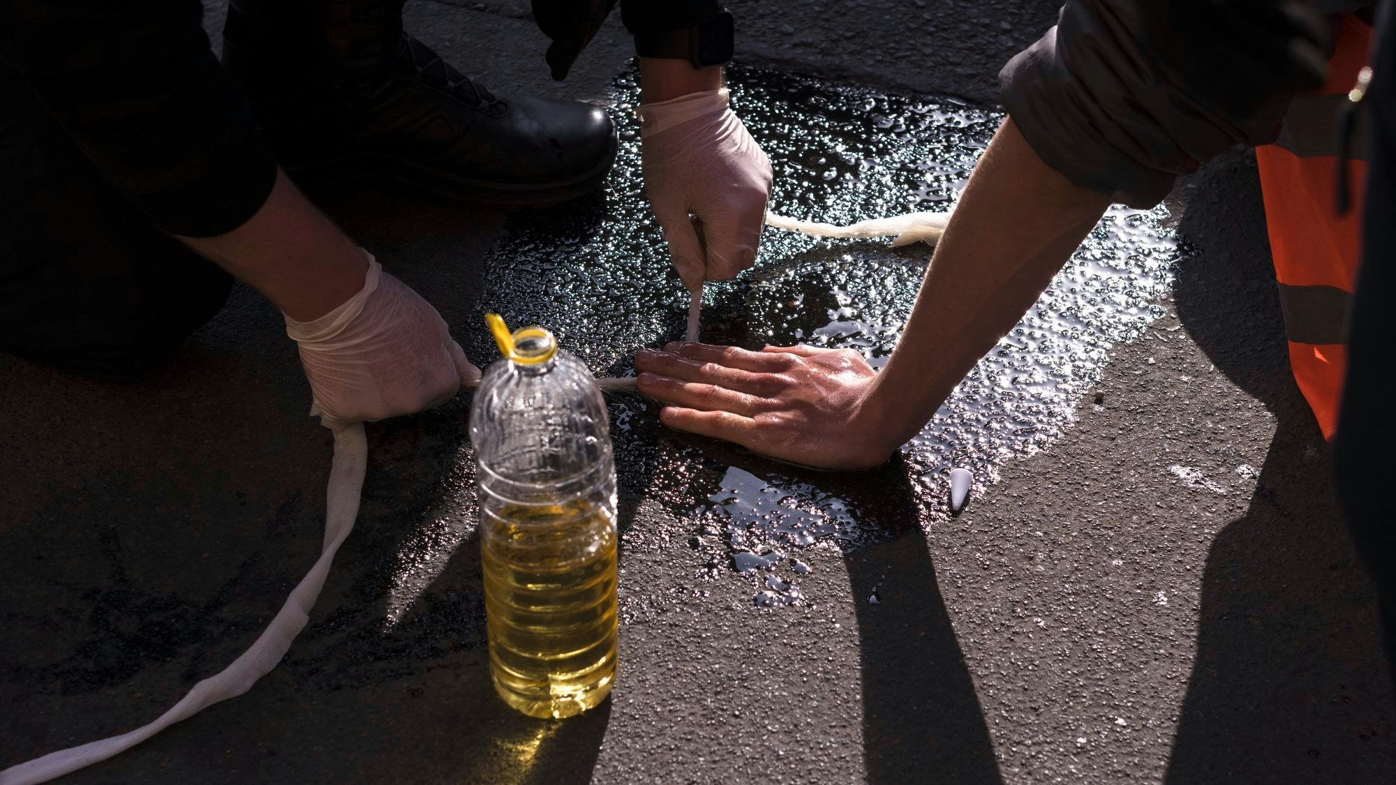 Polizeibeamte entfernen die Hand eines Aktivisten der Letzten Generation vom Asphalt.