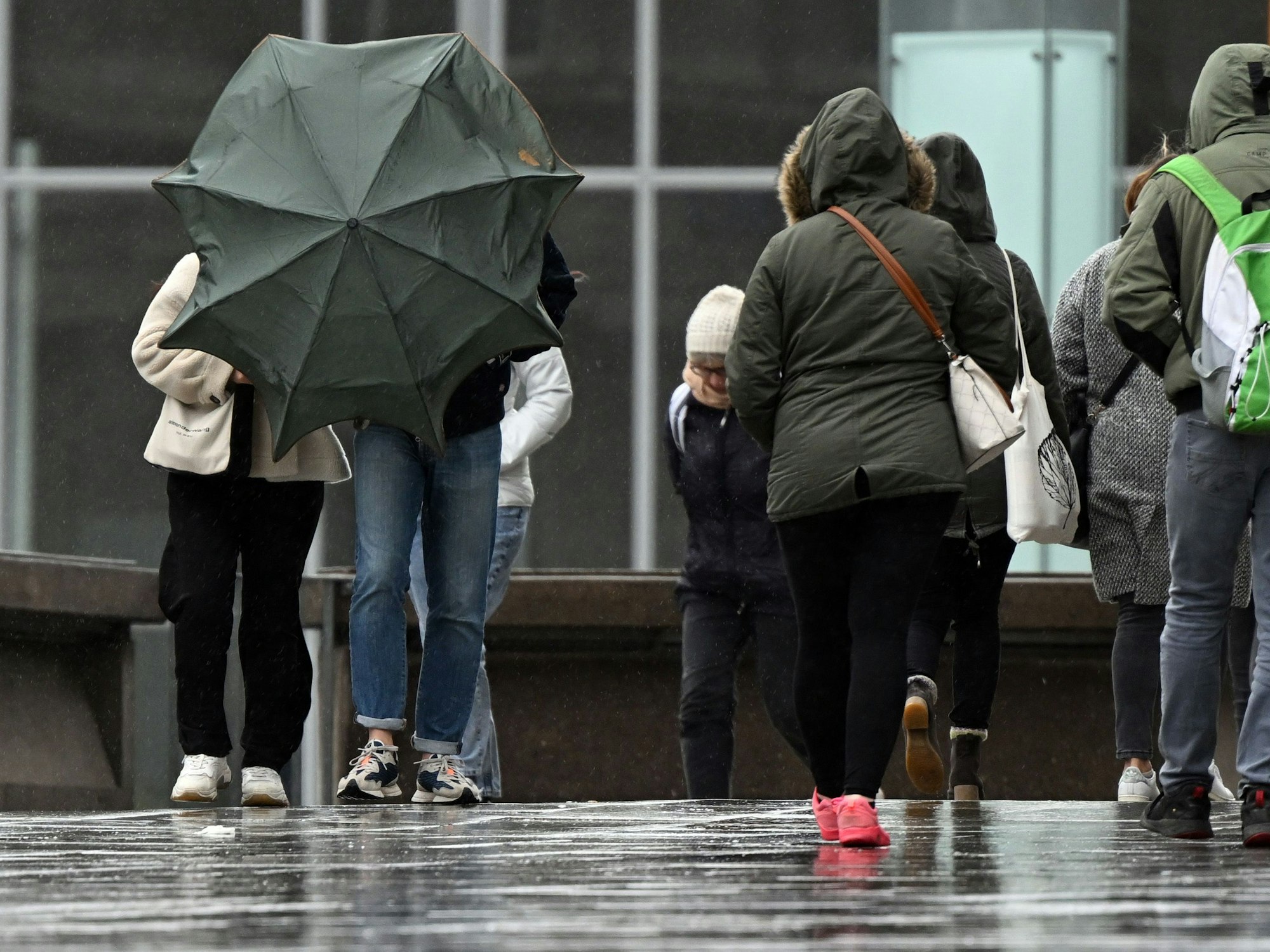 Spaziergänger kämpfen auf der Domplatte mit ihrem Regenschirm (Archivbild vom April 2022): Nach einem freundlichen Vormittag soll es am Sonntagnachmittag und -abend in NRW laut Vorhersage ungemütlich werden.