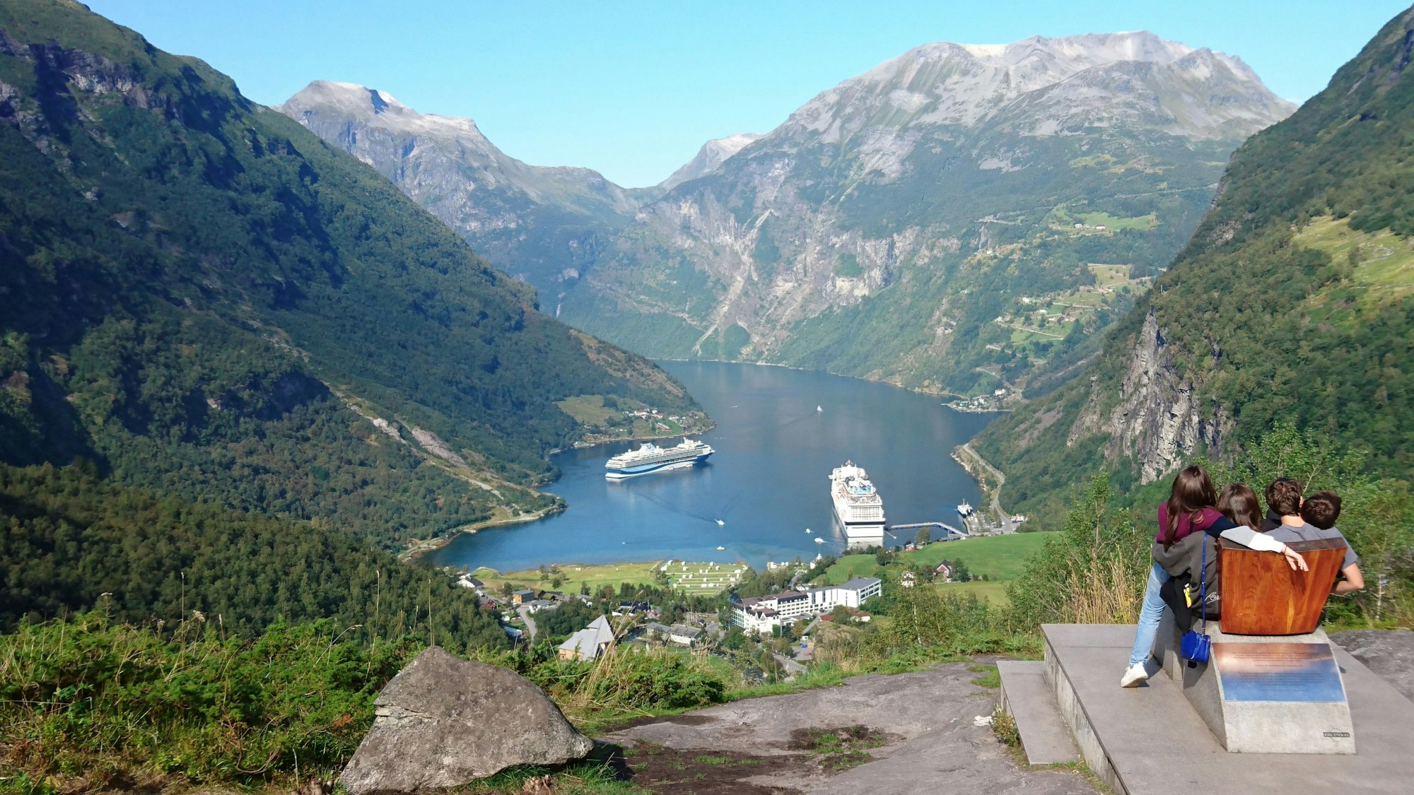 Personen schauen runter in den Geirangerfjord im Südwesten Norwegens auf die dort liegenden Kreuzfahrtschiffe.