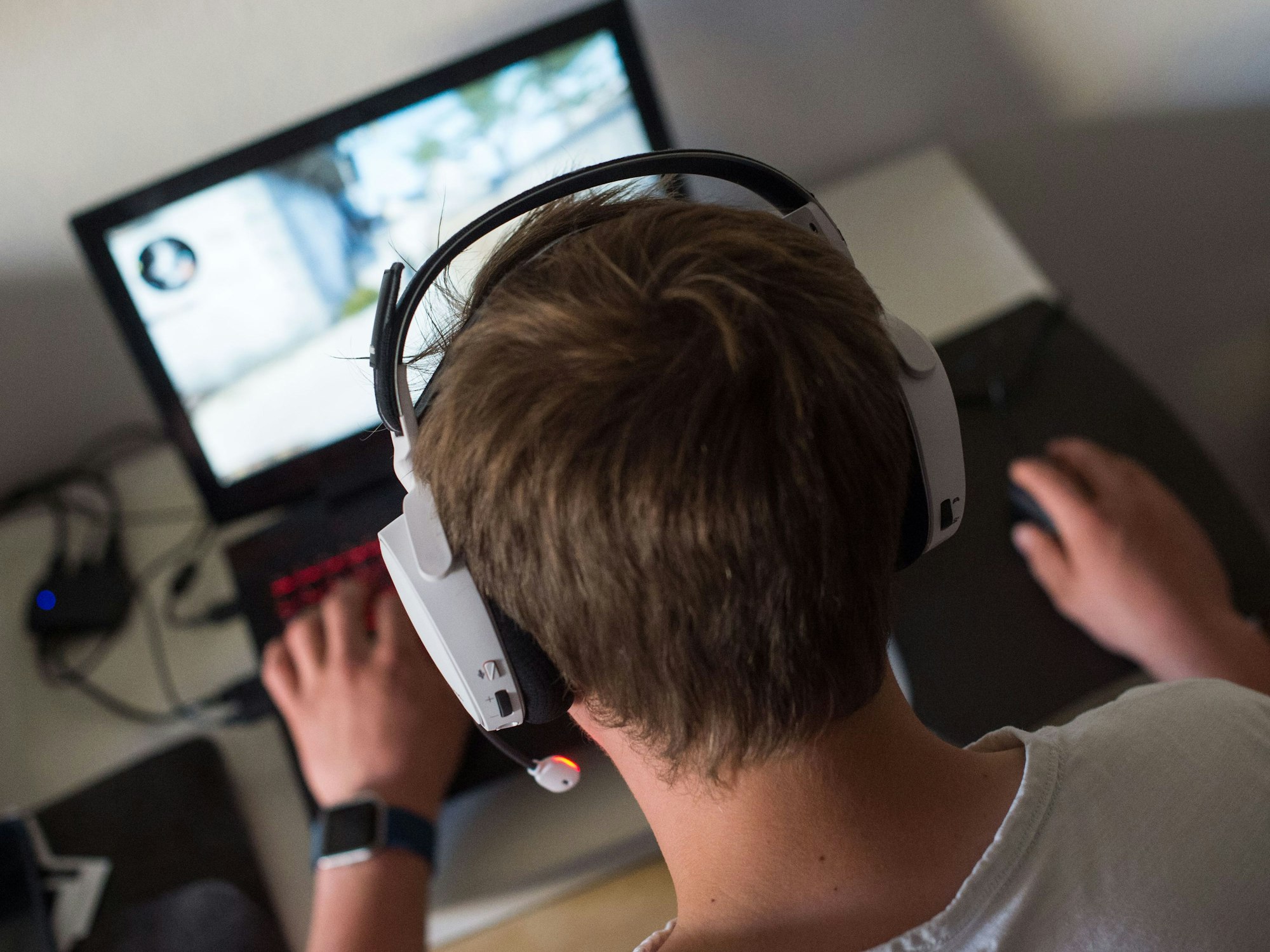 Ein Junge sitzt am mit einem Headset vor einem Laptop und spielt ein Online-Computerspiel.