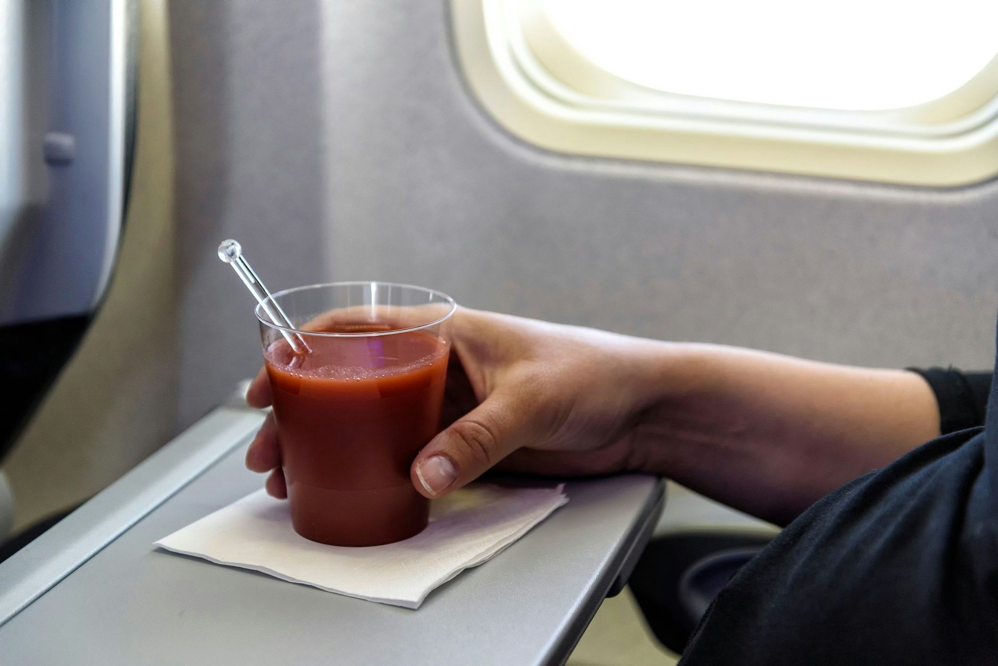 Eine Frau trink ein Glas Tomatensaft im Flugzeug.