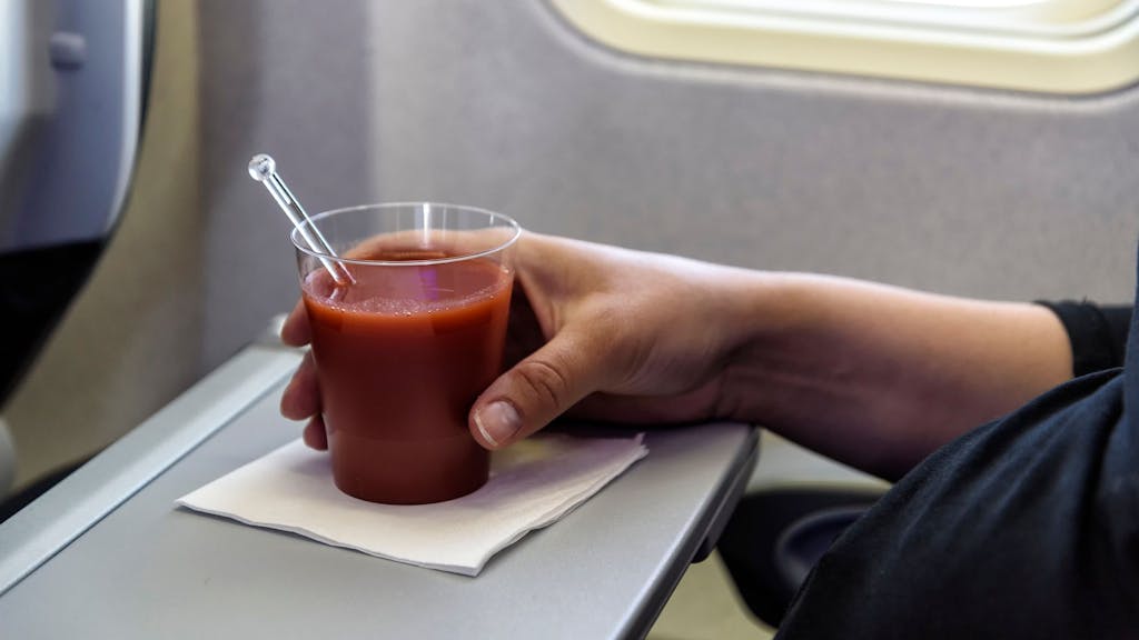 Eine Frau trink ein Glas Tomatensaft im Flugzeug.
