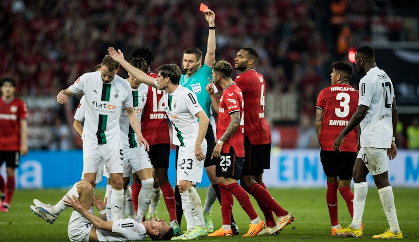 Gladbach-Star Julian Weigl liegt verletzt am Boden, Piero Hincapie von Bayer Leverkusen sieht nach seinem Foulspiel die Rote Karte (21. Mai 2023). Der Schiedsrichter hat den roten Karton in der Hand.