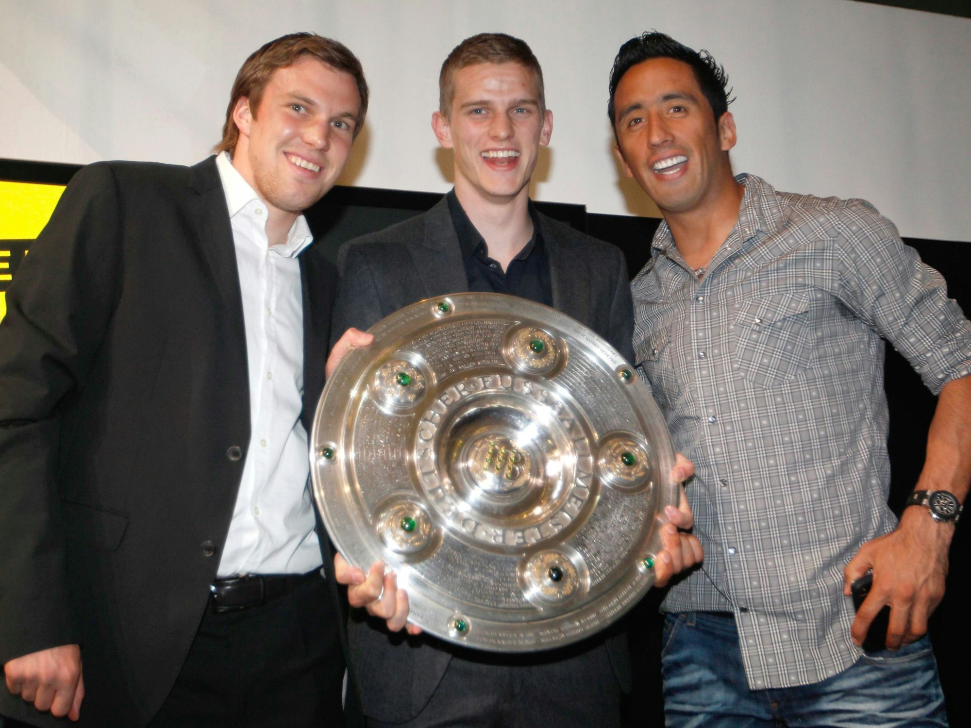 Kevin Großkreutz, Sven Bender und Lucas Barrios posieren mit der Schale, die Bender in den Händen hält. Alle drei Spieler lachen.