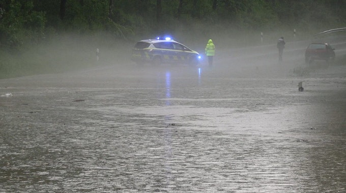 Schwere Unwetter in Detmold (Ostwestfalen-Lippe): Ein Polizist und ein Autofahrer stehen an einer überfluteten Straße nach dem Starkregen am Montagabend.