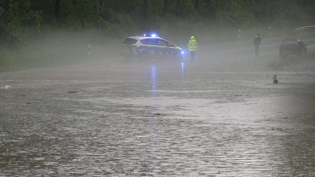 Ein Polizist und ein Fahrzeugfahrerstehen an einer überfluteten Straße bei Detmold.&nbsp;
