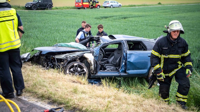 Drei Polizisten begutachten den zerstörten Audi. Auch die Feuerwehr war nach Unfall bei Kleinbüllesheim im Einsatz.