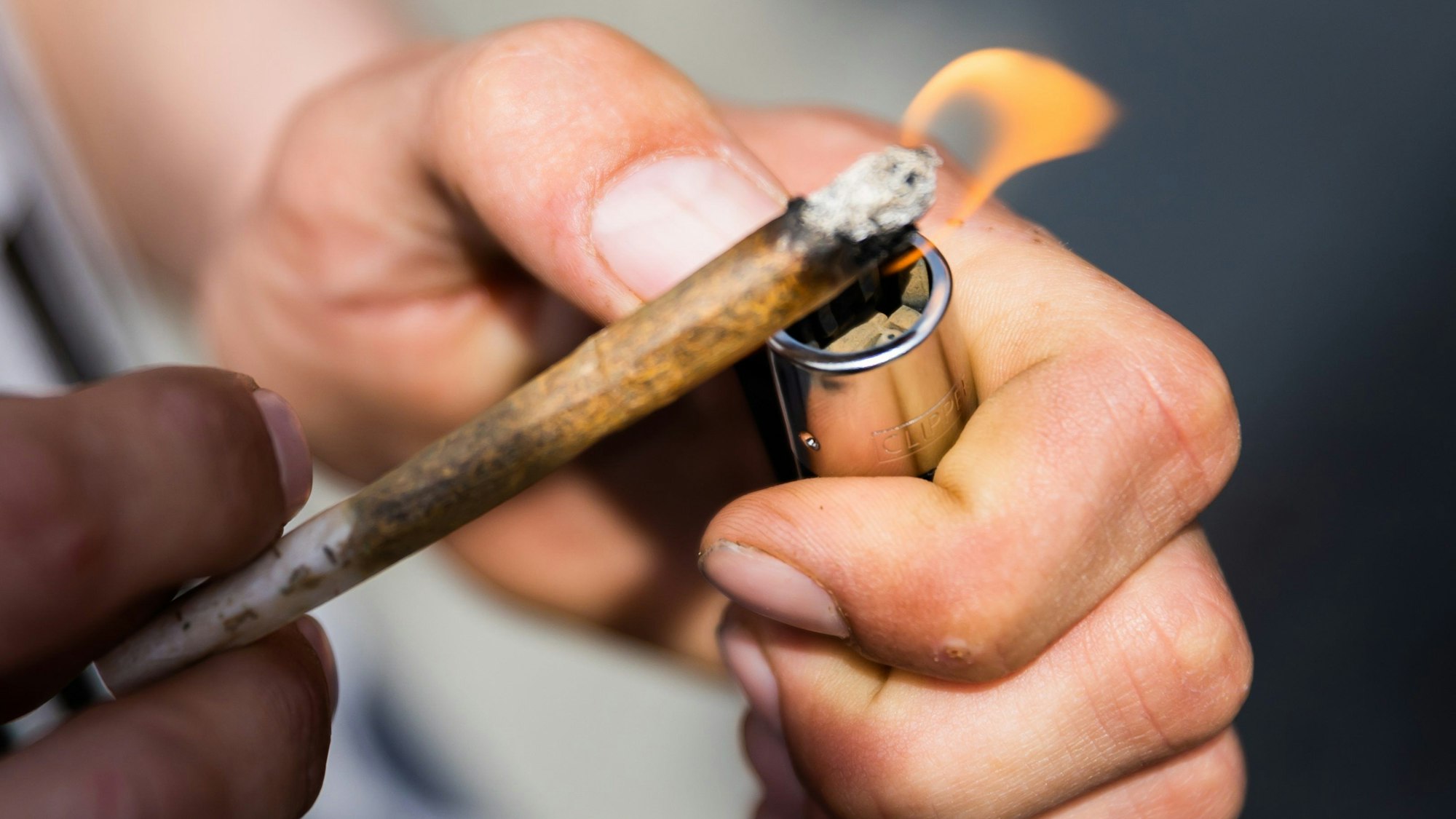 Ein Mann zündet einen Joint an. An der Idee, in NRW Modellstädte für die Cannabis-Abgabe zu benennen, scheiden sich in der schwarz-grünen Regierungskoalition die Geister. (Symbolbild)