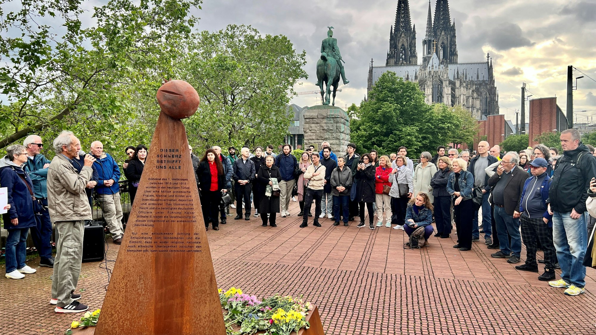 Kundgebung vor einem Mahnmal für den Genozid an Armeniern, im Hintergrund das Reiterdenkmal und der Kölner Dom.