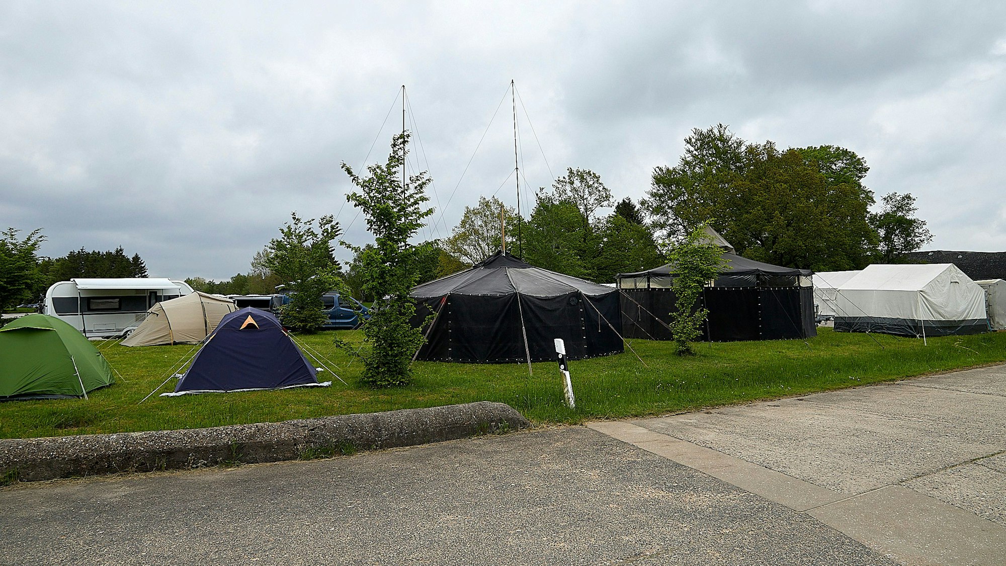 Das Bild zeigt mehrere kleine und drei größere Zelte, die auf einer Wiese aufgebaut sind.