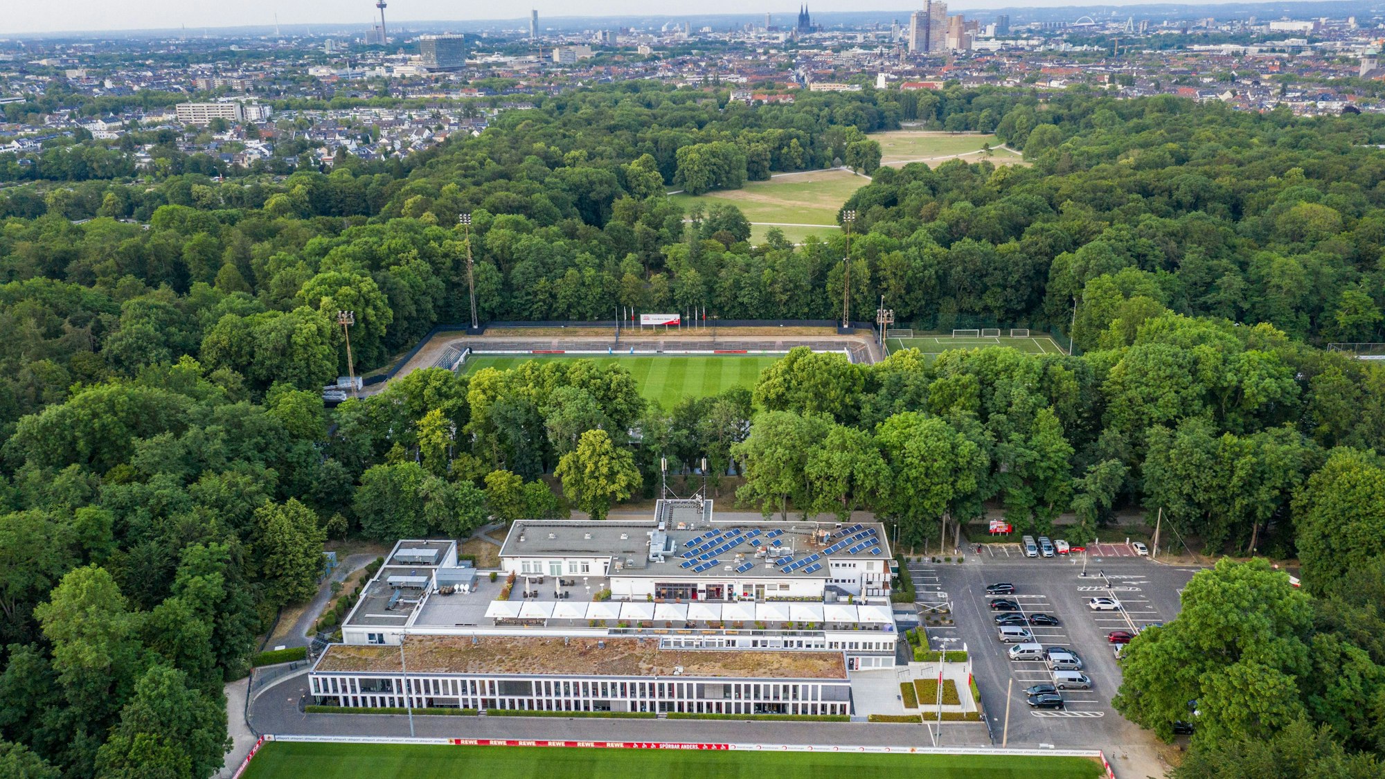 Das Geißbockheim genannte Clubhaus des Fußballverein 1. FC Köln mit dem Trainingsplatz 1 (vorne) und dem Franz-Kremer-Stadion (hinten) im Äußeren Grüngürtel. Im Hintergrund sind das Stadtzentrum und der Beethovenpark zu erkennen.