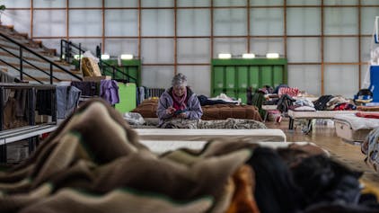 Eine ältere Frau sitzt auf einem Bett in einer Turnhalle, die als Unterkunft für Flutopfer dient.