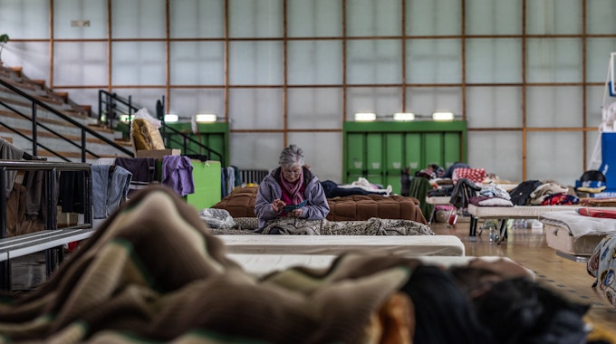 Eine ältere Frau sitzt auf einem Bett in einer Turnhalle, die als Unterkunft für Flutopfer dient.
