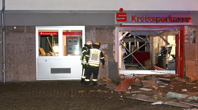 Feuerwehrleute stehen vor dem völlig zerstörten Eingangsbereich der Kreissparkasse in Kerpen-Türnich.