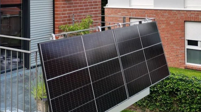 Zwei Solarmodule als Balkonkraftwerk sind an einem Gitterbalkon angebracht.