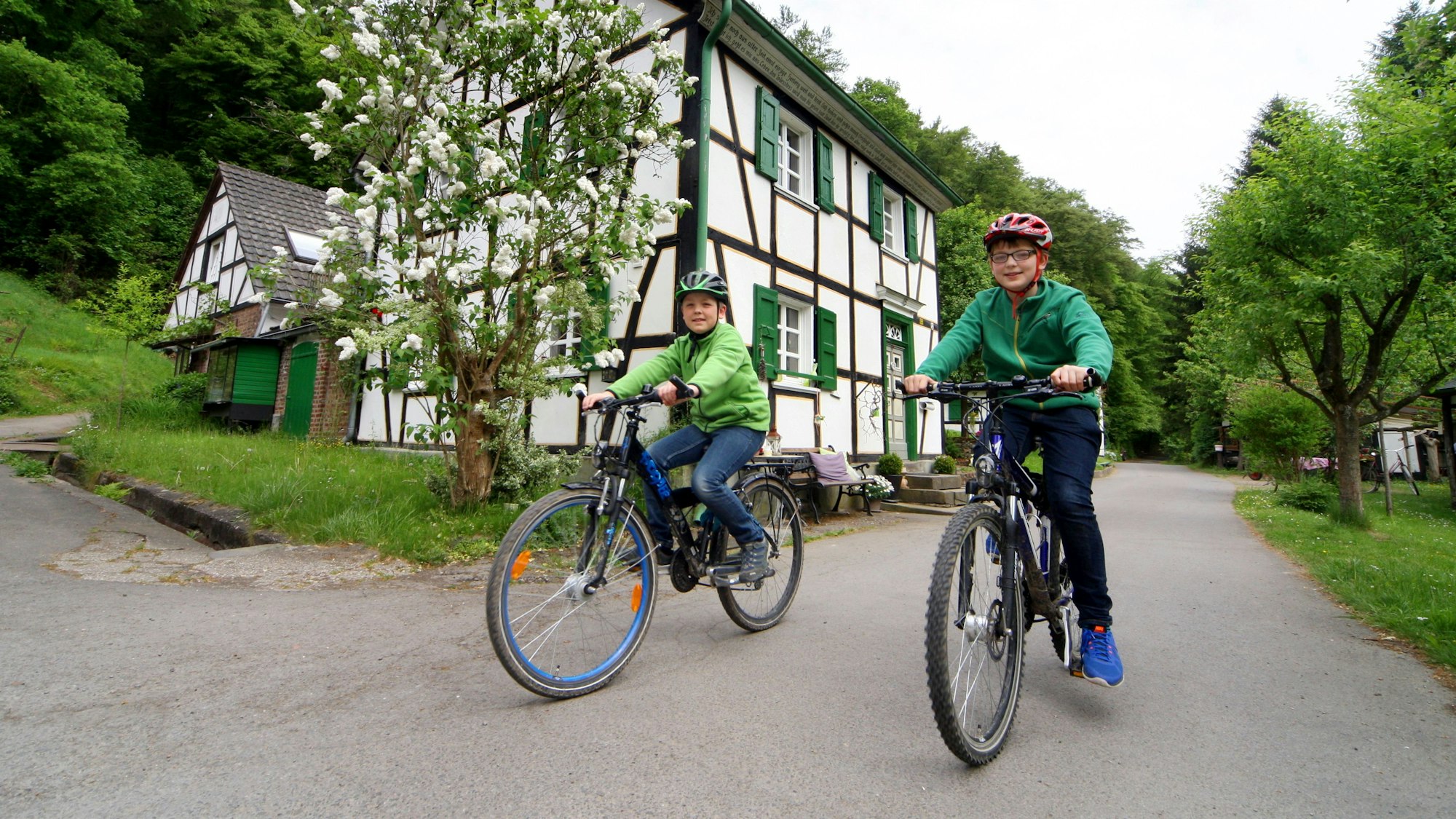 Unten am Mühlenweg ist die Radwelt noch in Ordnung, aber von hier führen nur steile Wanderwege hinauf nach Glöbusch. Zwei Kinder sitzen auf Fahrrädern.